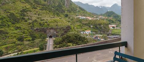 A balcony with two cups and a chair, overlooking a road with a tunnel and a mountainous landscape.