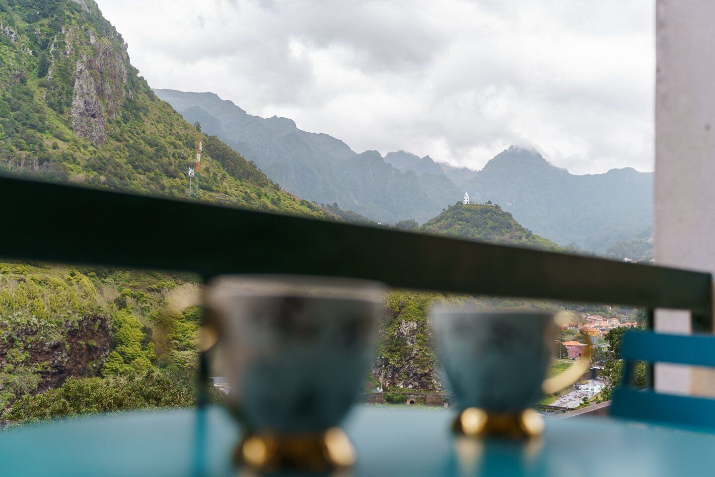 Vista desde una ventana sobre un paisaje montañoso con un pequeño pueblo abajo.