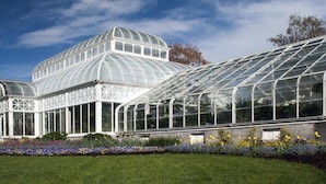 A large greenhouse with a glass roof and walls, surrounded by a well-maintained garden.