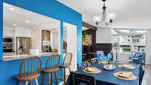 A modern kitchen with white cabinets, a blue accent wall, and a dining area with a table set for four.
