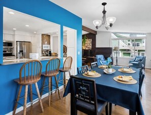 Une cuisine moderne avec des meubles blancs, un mur d’accent bleu et un coin repas avec une table dressée pour quatre personnes.