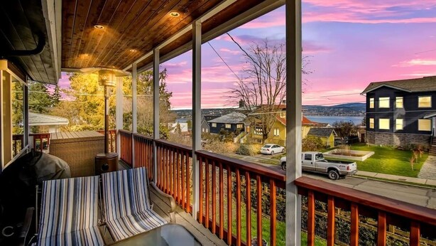 A covered porch with a view of a residential neighborhood and a body of water during sunset.