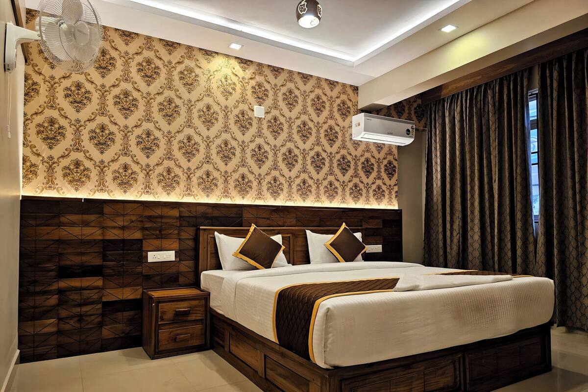 A modern bedroom with a patterned wallpaper, a wooden headboard, a bed with white bedding, a nightstand, and an air conditioning unit.