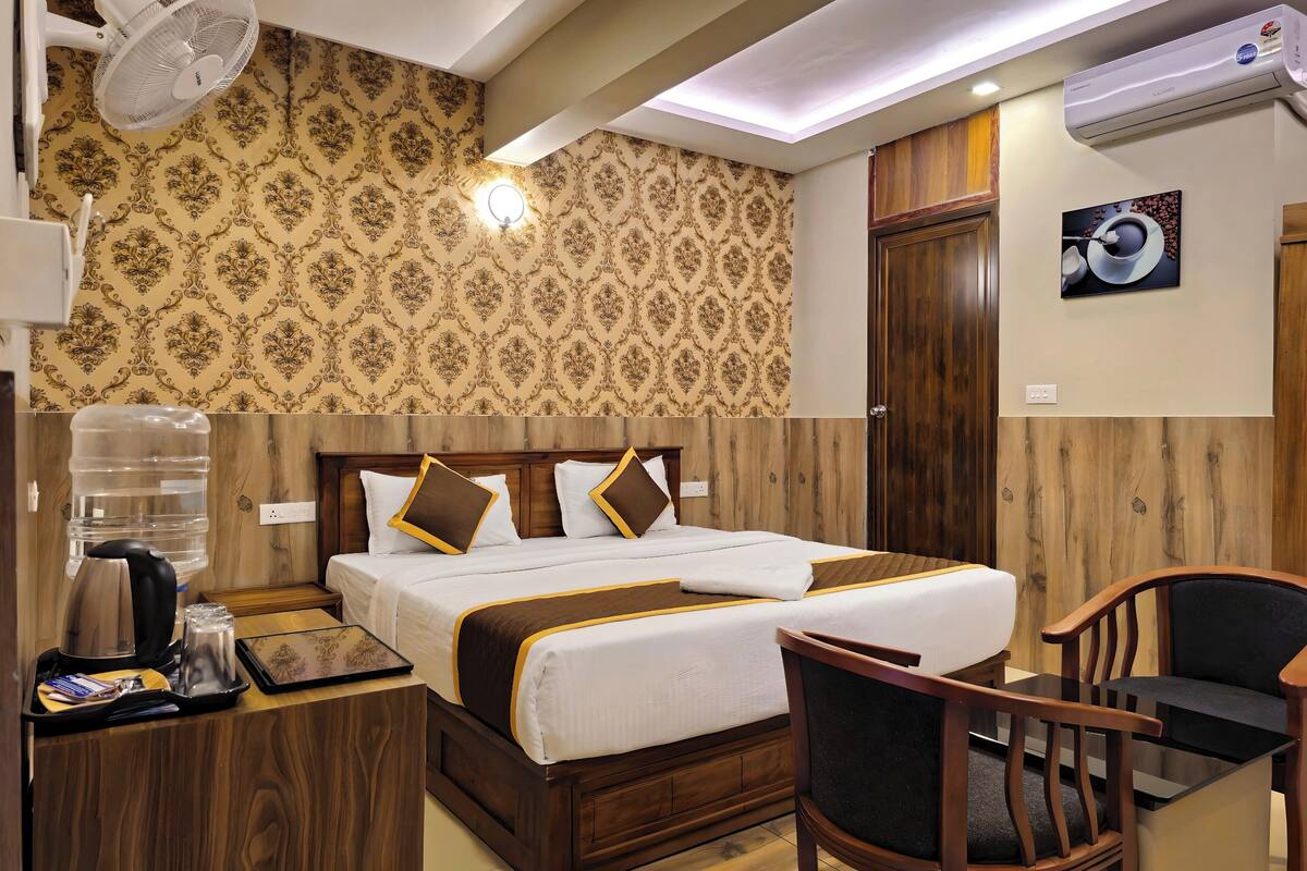 A hotel room with a bed, bedside table, chair, and a large water dispenser.