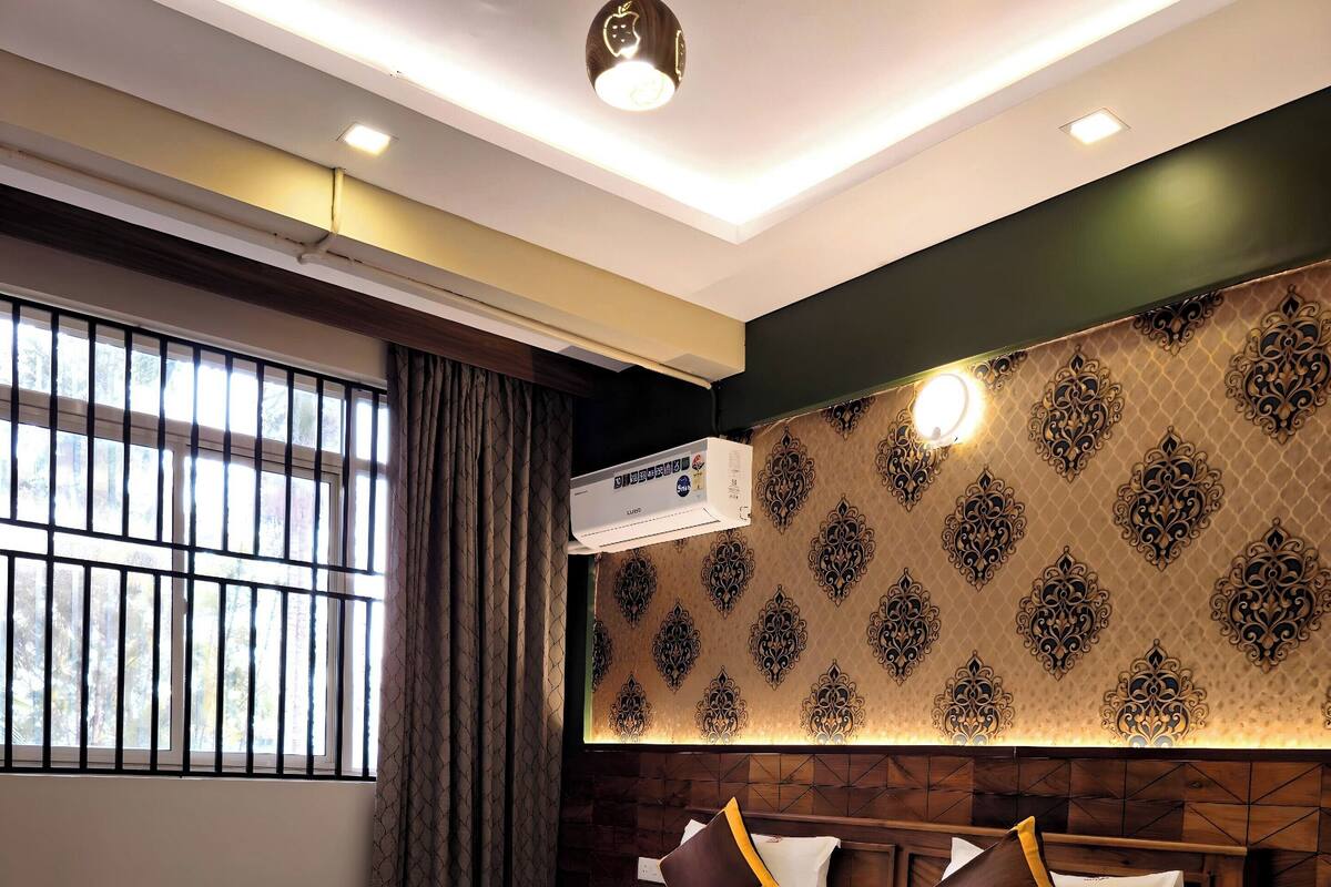 A hotel room with a large bed, wooden headboard, patterned wallpaper, and a window with bars.
