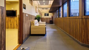 A hotel lobby with a reception desk, seating area, and large windows. - Alicos Residency (Sulthan Bathery)