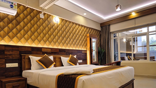 A modern hotel room with a large bed, wooden headboard, and a view of the outdoors through a window. - Alicos Residency (Sulthan Bathery)