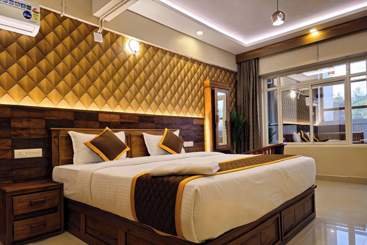 A modern hotel room with a large bed, wooden headboard, and a view of the outdoors through a window.