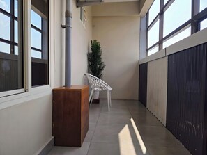 A corridor with a wooden bench, a white chair, and a potted plant. - Alicos Residency (Sulthan Bathery)