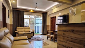 A modern living room with a leather sofa, a wooden cabinet, and a TV mounted on the wall. - Alicos Residency (Sulthan Bathery)