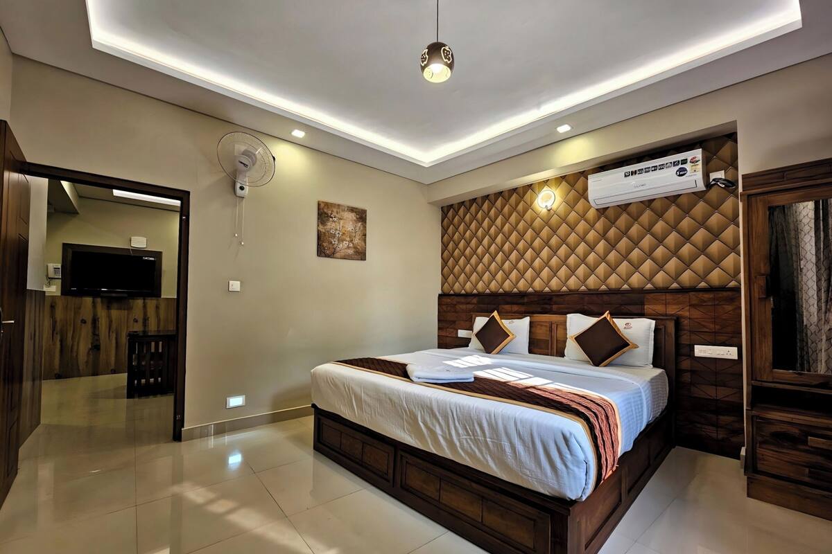 A modern hotel room with a large bed, a flat-screen TV, a ceiling fan, and a wall-mounted air conditioner.