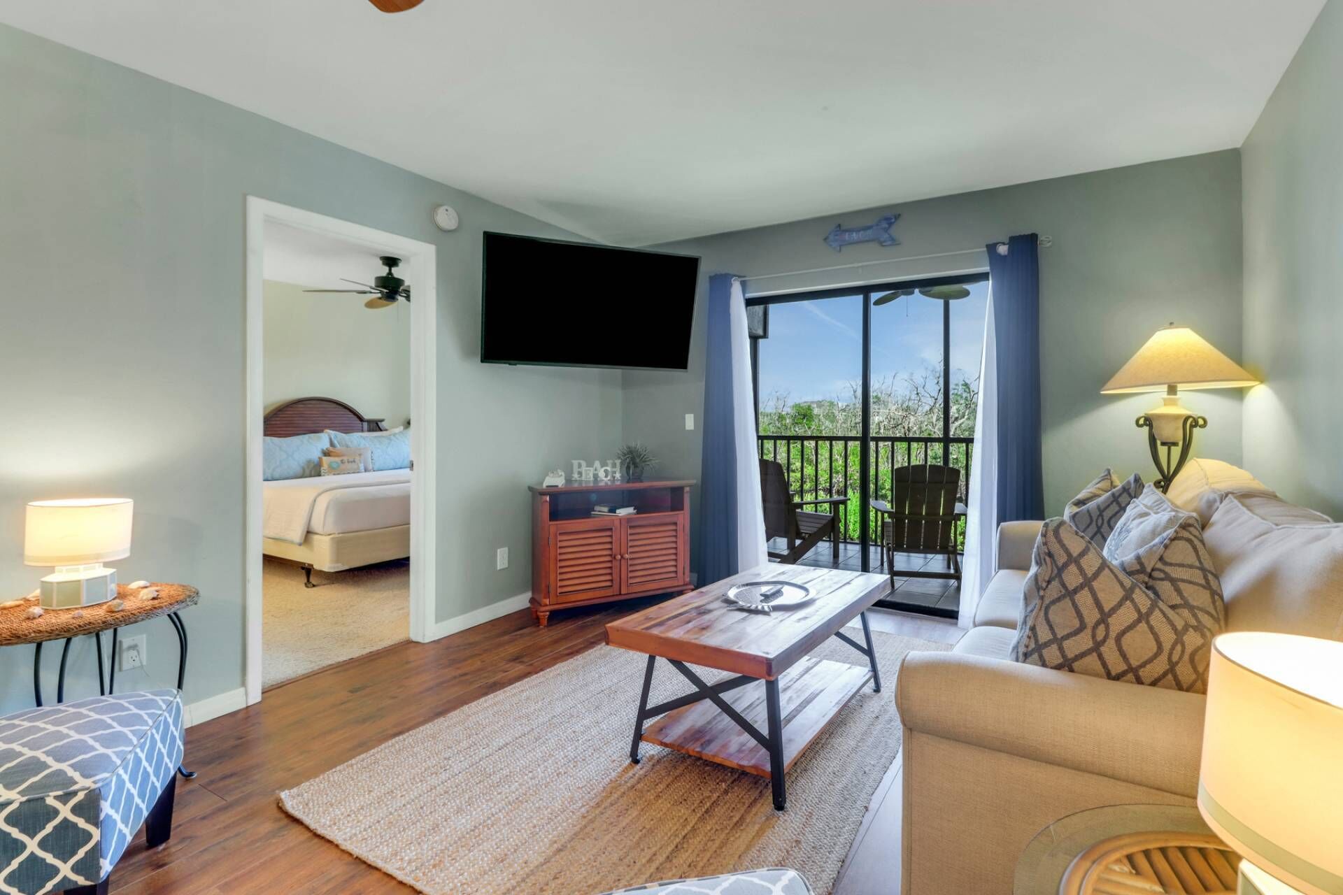 A living room with a sofa, a coffee table, a TV, a bed, and a balcony with a view.