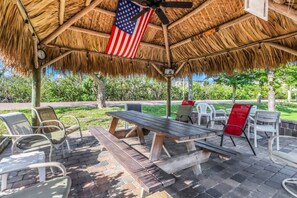 Een terras buiten met rieten dak, een vlag en een klok.