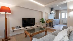 Ein modernes Wohnzimmer mit Flachbildfernseher, Glastisch, Sofa und Stehlampe.