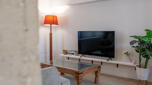 Ein modernes Wohnzimmer mit einem Glastisch, einem Fernseher auf einem Lowboard, einer Stehlampe und einem Blumentopf.