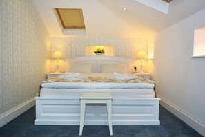 A bedroom with a large bed, two bedside tables, a small stool, and a skylight.
