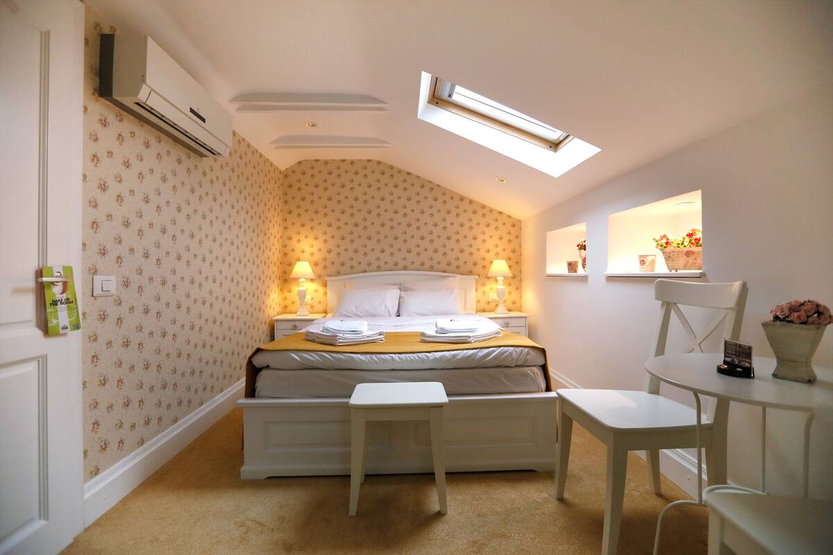 A bedroom with a bed, bedside tables, a small table, a chair, and a mirror.