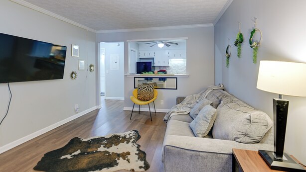 A living room with a sofa, a flat-screen TV, a wooden floor, and a kitchen in the background. - < 1 Mi to Vanderbilt: Nashville Apt (Nashville)
