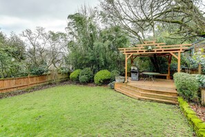 A backyard with a wooden pergola, a barbecue area, and a small deck. - Charming Tudor-Style Apt Near Green Lake! (Seattle)