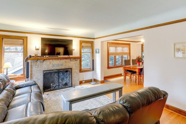 A living room with a fireplace, leather sofa, and a dining area with a table and chairs. - Charming Tudor-Style Apt Near Green Lake! (Seattle)