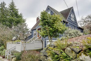 A two-story house with a steeply pitched roof, a front porch, and a stone retaining wall. - Charming Tudor-Style Apt Near Green Lake! (Seattle)