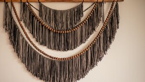 A macrame wall hanging with multiple layers of fringes and wooden beads. - NHOA 312B Lux 1BR in Aldea Zama (Tulum)