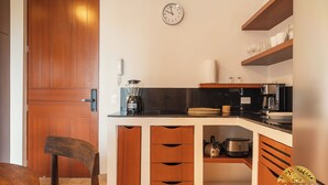 A compact kitchen with wooden cabinetry, a black countertop, and a clock on the wall. - NHOA 312B Lux 1BR in Aldea Zama (Tulum)