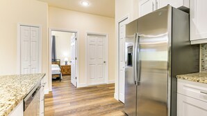 Une cuisine avec un plancher en bois, des armoires blanches et un réfrigérateur en acier inoxydable.