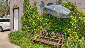 Un edificio con una gran escultura de pez, un banco y un coche aparcado cerca.
