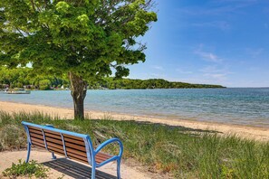 Un banc au bord d’un lac, avec un arbre, un ciel dégagé et une rive lointaine.