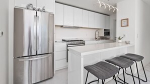 Een moderne keuken met een roestvrijstalen koelkast, witte kasten, een centraal kookeiland met barstoelen en een hanglamp.