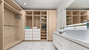 Een moderne badkamer met een grote spiegel, een witte wastafel en een inloopkast met houten planken.