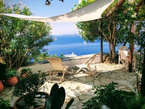 Un patio con pavimento in pietra, due sedie di legno, un tavolo e vista sul mare.