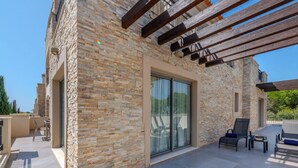 Un bâtiment moderne avec une façade en pierre, de grandes portes coulissantes en verre et un patio couvert doté d’un espace salon extérieur.