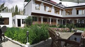 Uma casa de dois andares com varanda coberta, um jardim com diversas plantas e mobiliário de exterior.