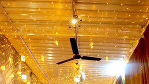 Un restaurant doté d’un ventilateur de plafond, de guirlandes lumineuses et d’une scène. Des tables et des chaises sont disposées pour accueillir les clients.