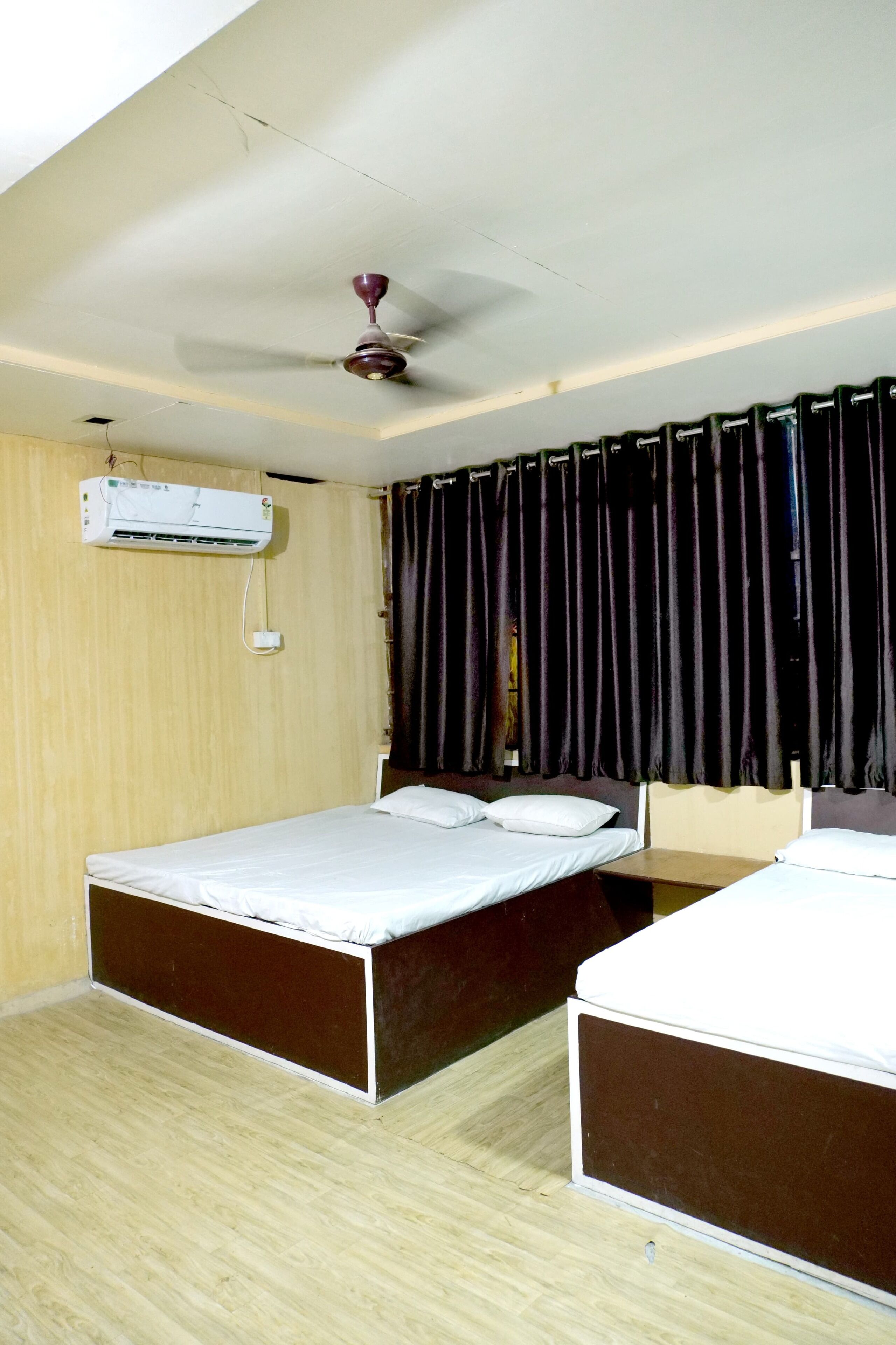 A room with two single beds, a ceiling fan, an air conditioning unit, and dark curtains.