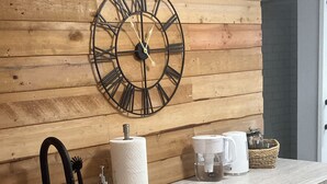 Una cocina con pared de madera, un reloj grande, un lavamanos, una cafetera y armarios.