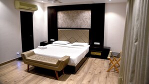 A modern bedroom with a large bed, bedside tables, a bench, and an air conditioning unit.