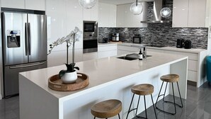A modern kitchen with a large island, stainless steel appliances, and pendant lighting.