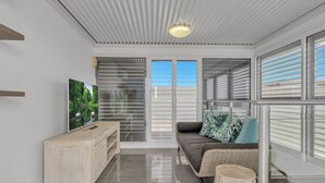 A modern living room with a sofa, a wooden bench, a television, and a large window with blinds.