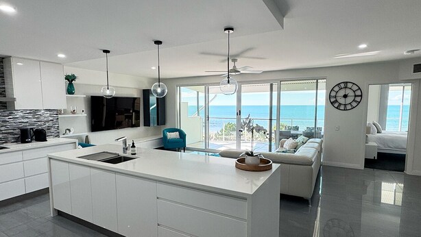 A modern kitchen with a large island, white cabinetry, and a view of the ocean.