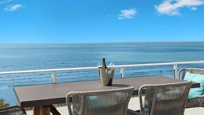 An outdoor seating area with a table and wicker chairs, overlooking a body of water.