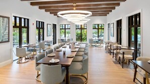 A spacious conference room with long tables and chairs, large windows, and a modern ceiling light fixture.