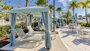 A covered outdoor seating area with chairs and a canopy, surrounded by palm trees and a white fence.