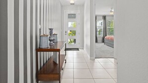 A hallway with a striped wall, a wooden bench with decorative items, and a door leading to a room with a bed and a window.