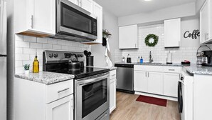 Une cuisine moderne avec des meubles blancs, une cuisinière en acier inoxydable, un four à micro-ondes, une bouilloire et un lave-vaisselle.