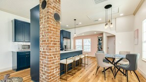 A modern kitchen with a brick column, dark blue cabinets, and a central island with bar stools.