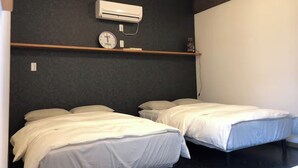 A room with two single beds, a wall-mounted air conditioner, a clock, and a shelf with a small decorative item. - GoodHome Toyokawa (Hakodate)