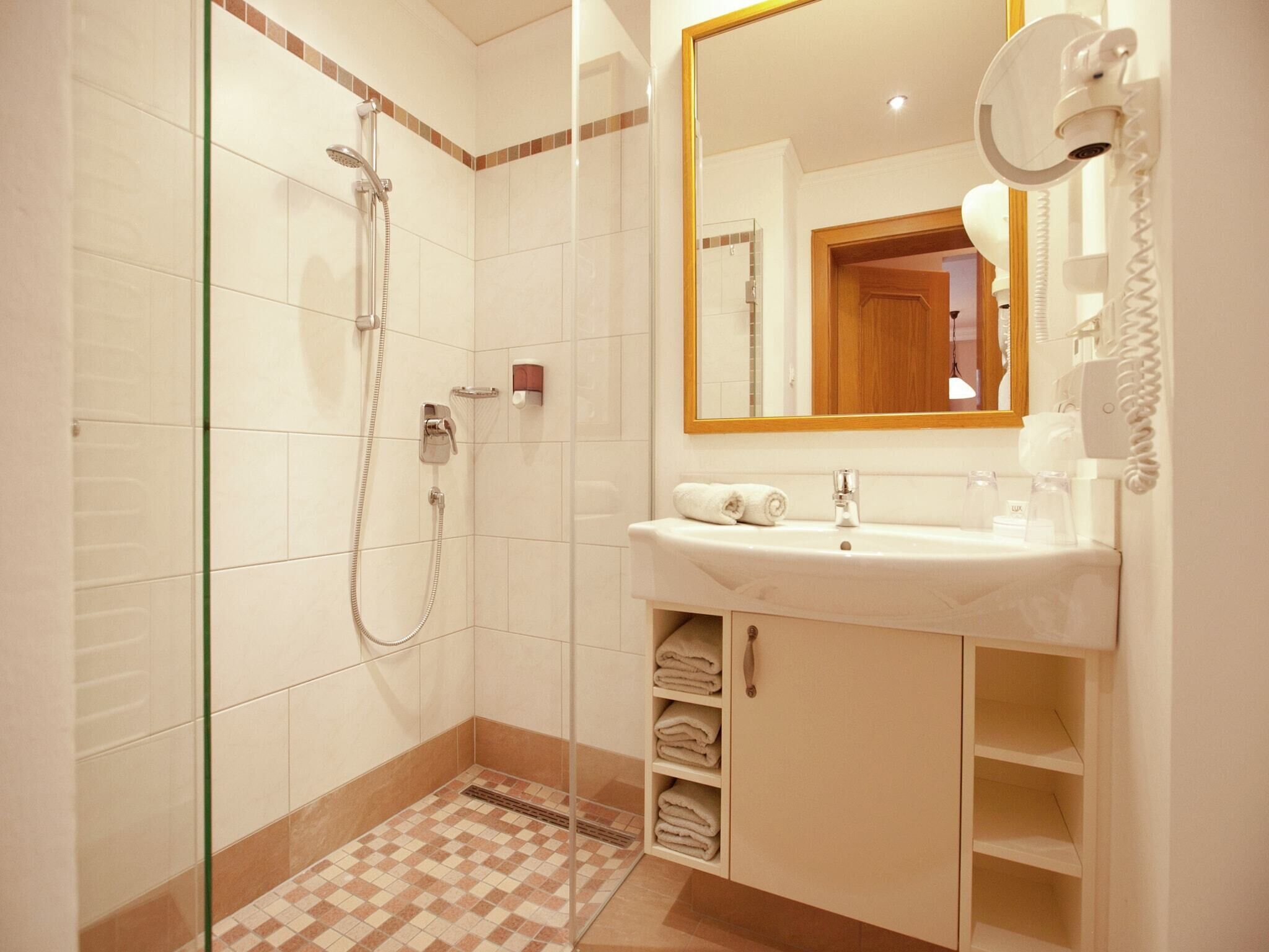Uma casa de banho moderna com chuveiro em cabine de vidro, lavatório branco com espelho e porta-toalhas.